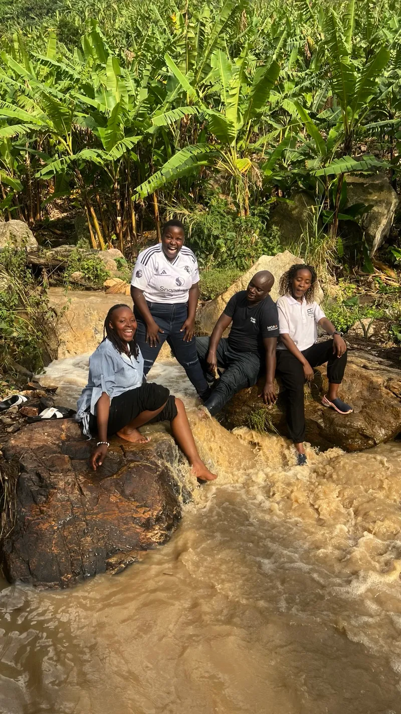 Four people sitting beside a fast-flowing silt-laden stream below banana cultivation