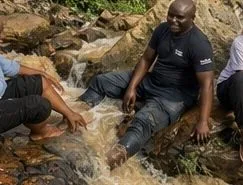 Two people sitting on wet rock beside running water at the source